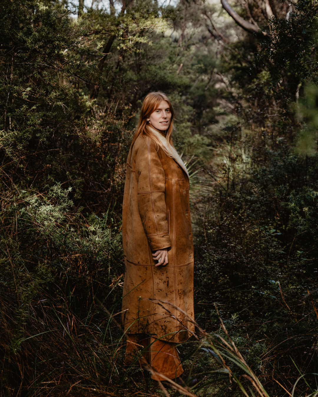Tahi brand portrait of woman in long brown leather coat standing in lush native forest