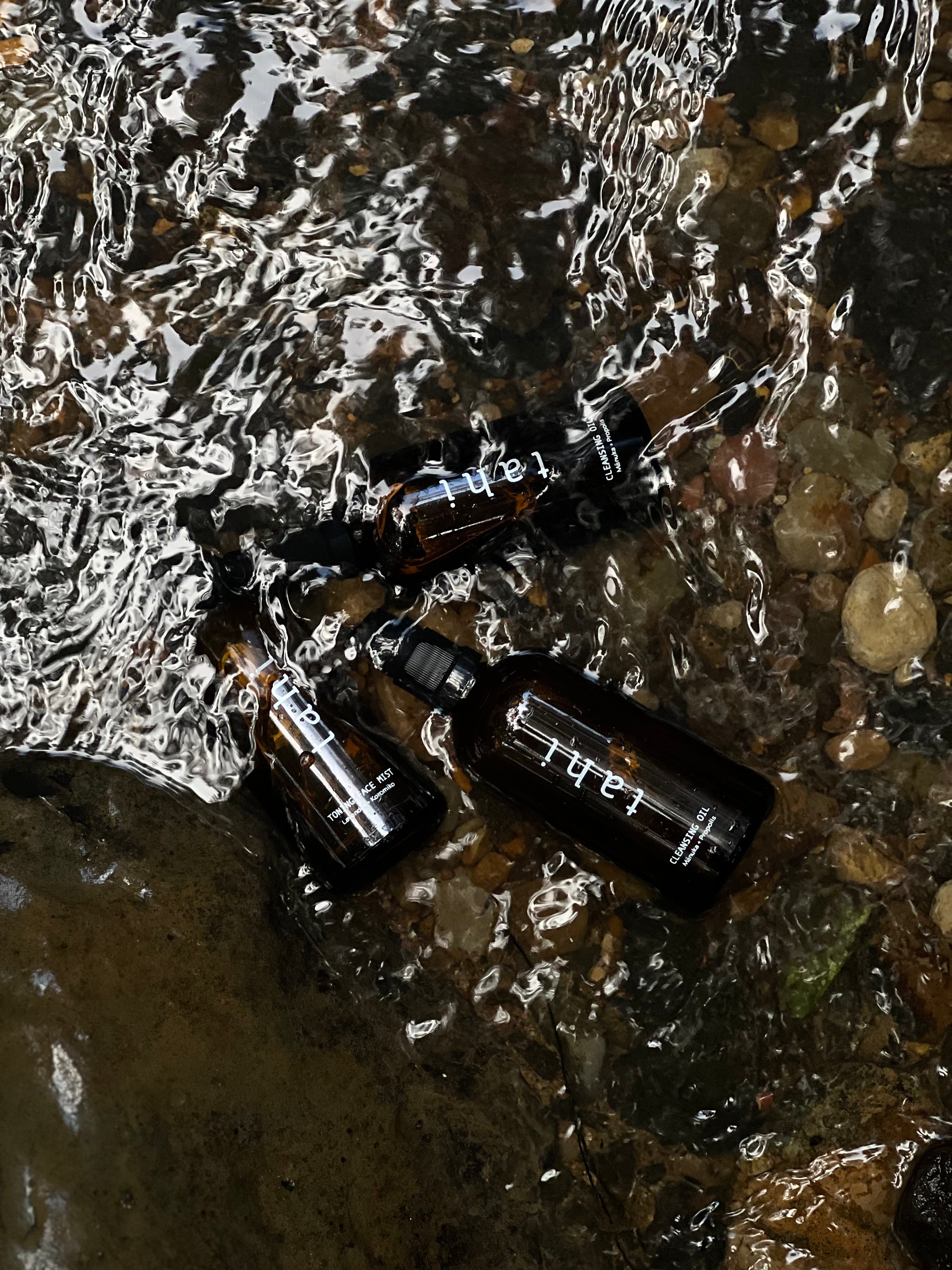 Tahi three product bottles partially submerged in rocky river